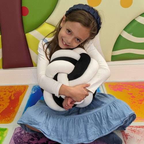 Black and white knot ball cuddle cushion hugged in arms, plush knot pattern