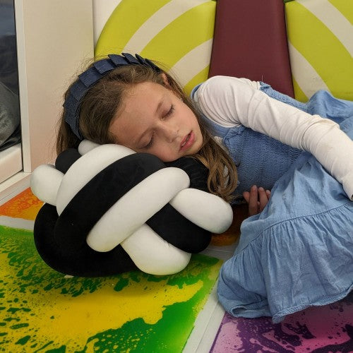 Black and white knot ball cuddle cushion cradled while resting, plush knot loops