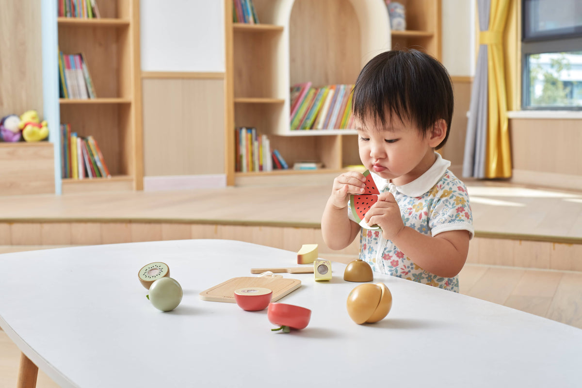 Wooden fruit cutting toy pieces on table, child holding watermelon slice