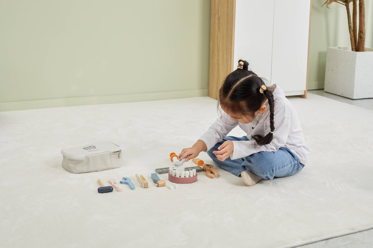 Dentist playset on floor with toy tools and mouth model while a child plays