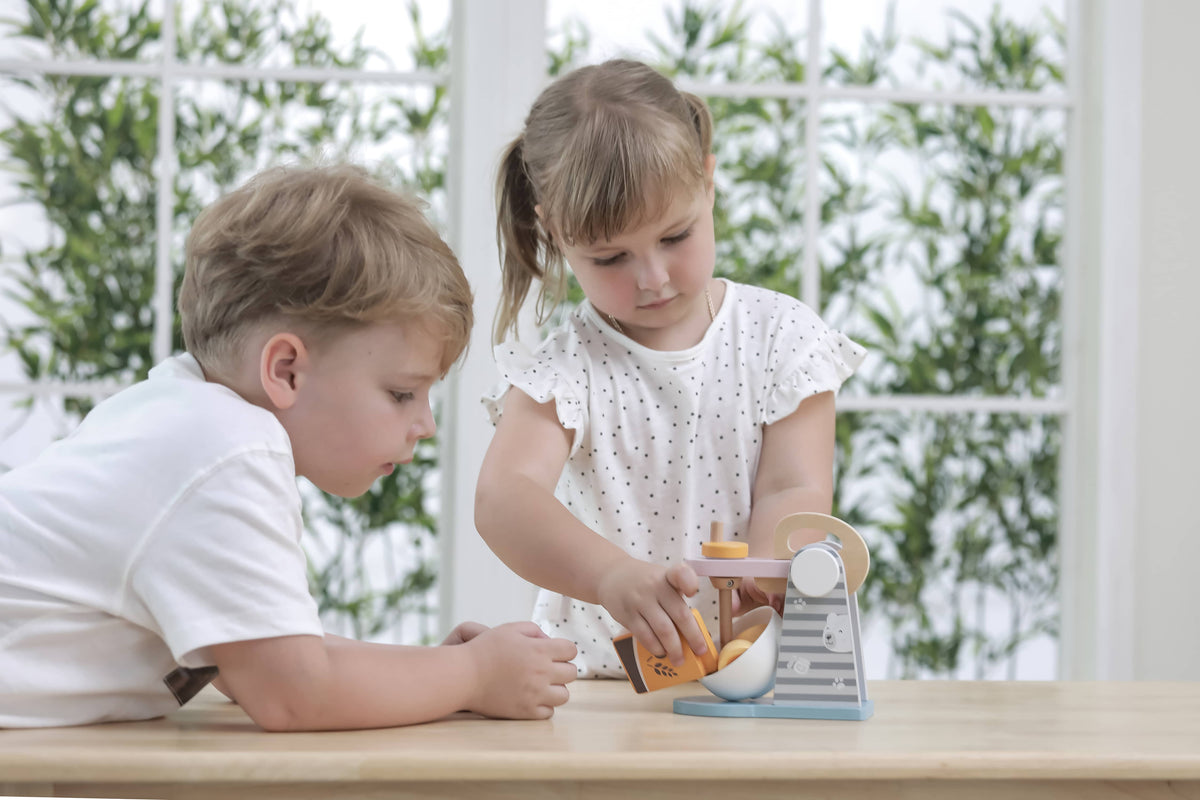 Kids playing with wooden toy mixer set, bowl, and small accessories on table