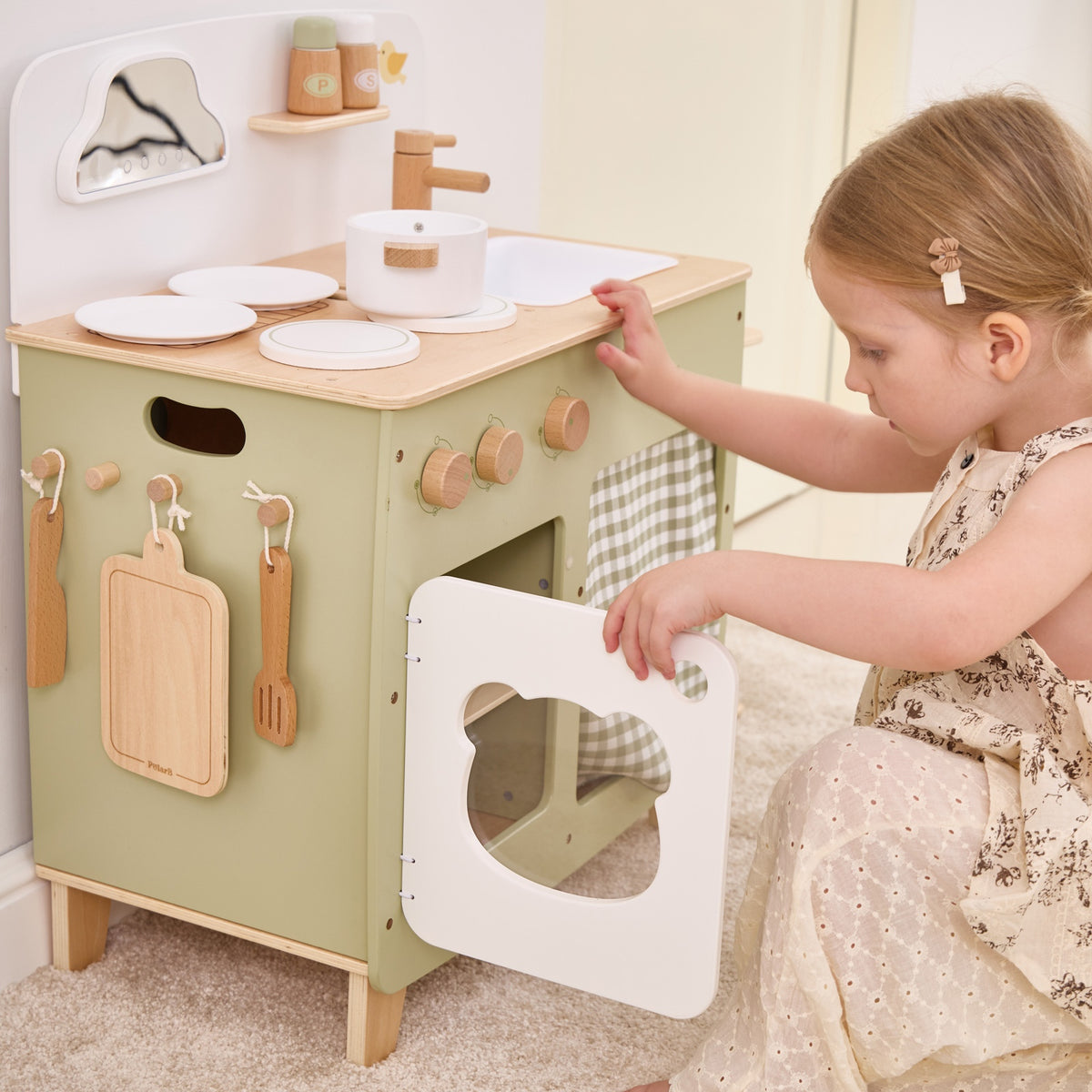 Wooden play kitchen with open oven door, hanging utensils, and food play pieces