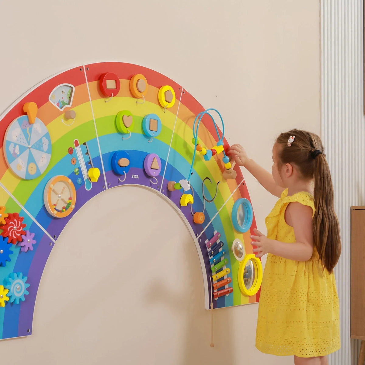 Rainbow activity wall panels with child reaching for spinning and stacking toys