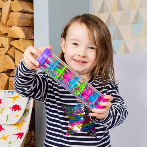 Kids' rainmaker toy held in hand: purple capped clear cylinder with colorful beads