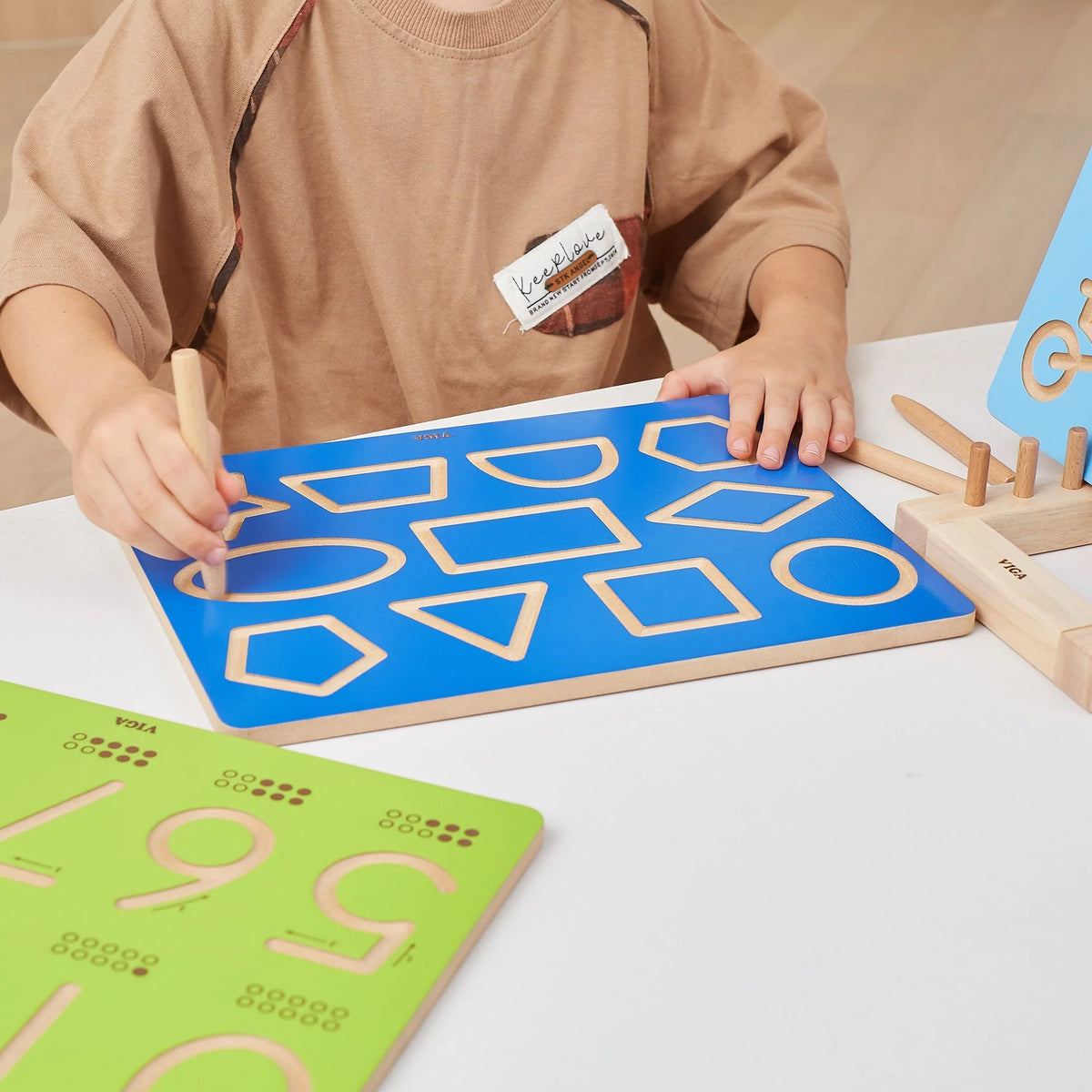Blue shapes tracing board with cutout outlines, held by hands with wooden tracing stylus