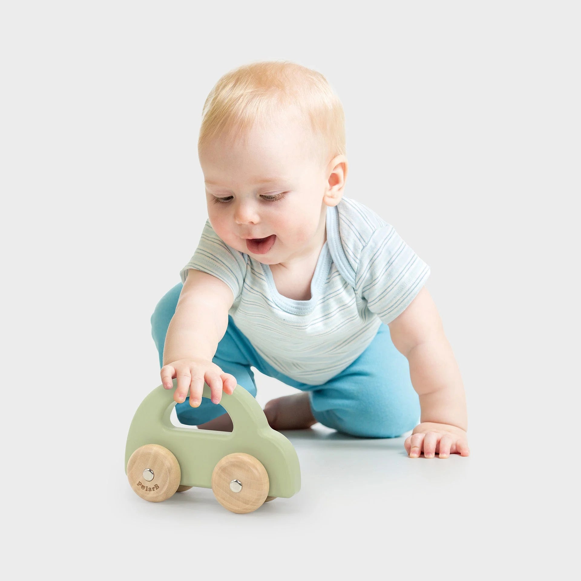 Baby kneeling and playing with green wooden toy car with wooden wheels