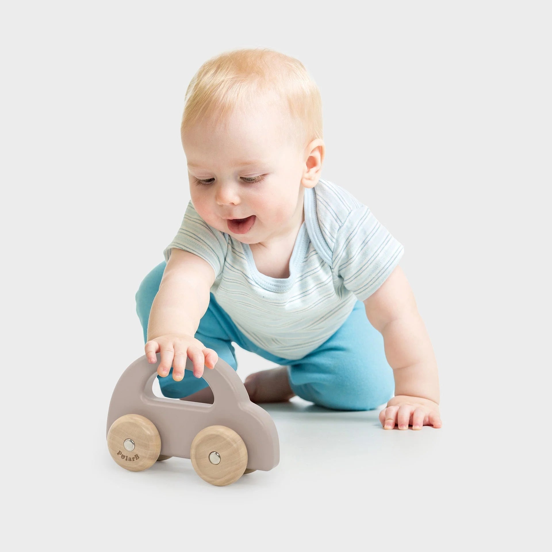 Light brown wooden toy car with 2 round wheels, held by baby in striped shirt