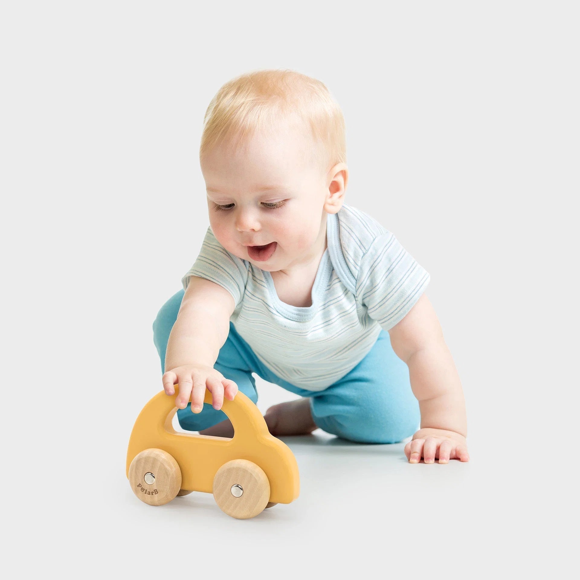 Yellow wooden toy car with wooden wheels, baby hands reaching toward it