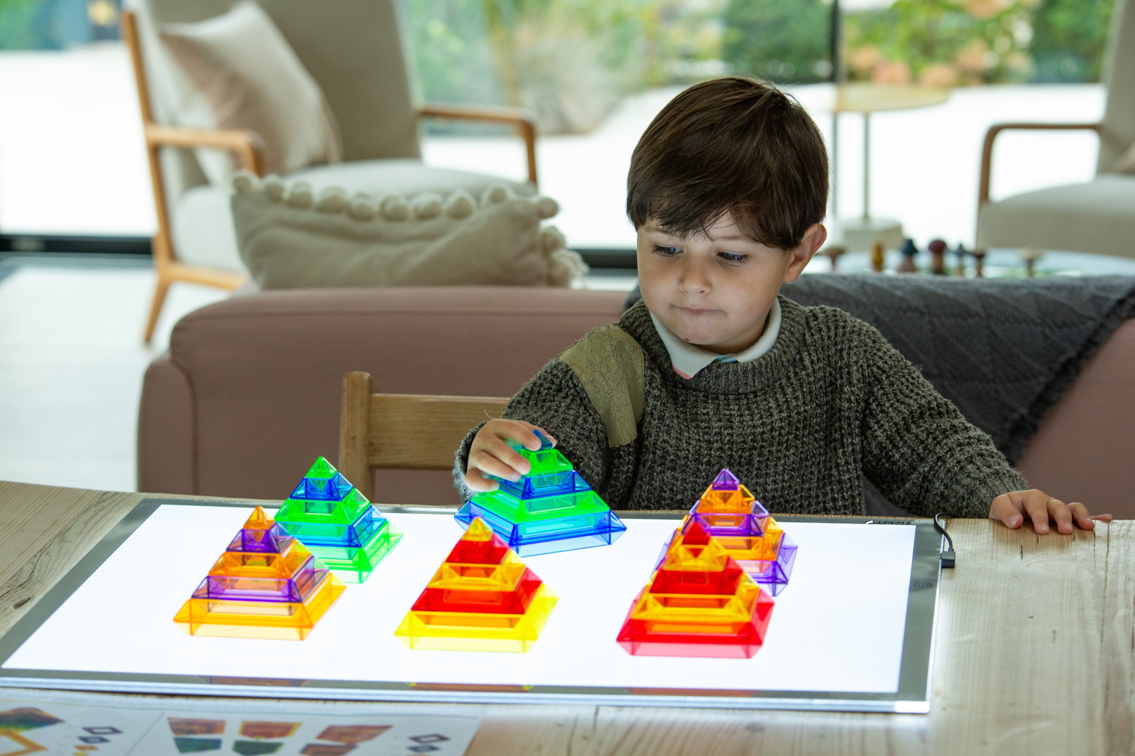 Child playing with rainbow pyramid blocks on a glowing light panel tabletop