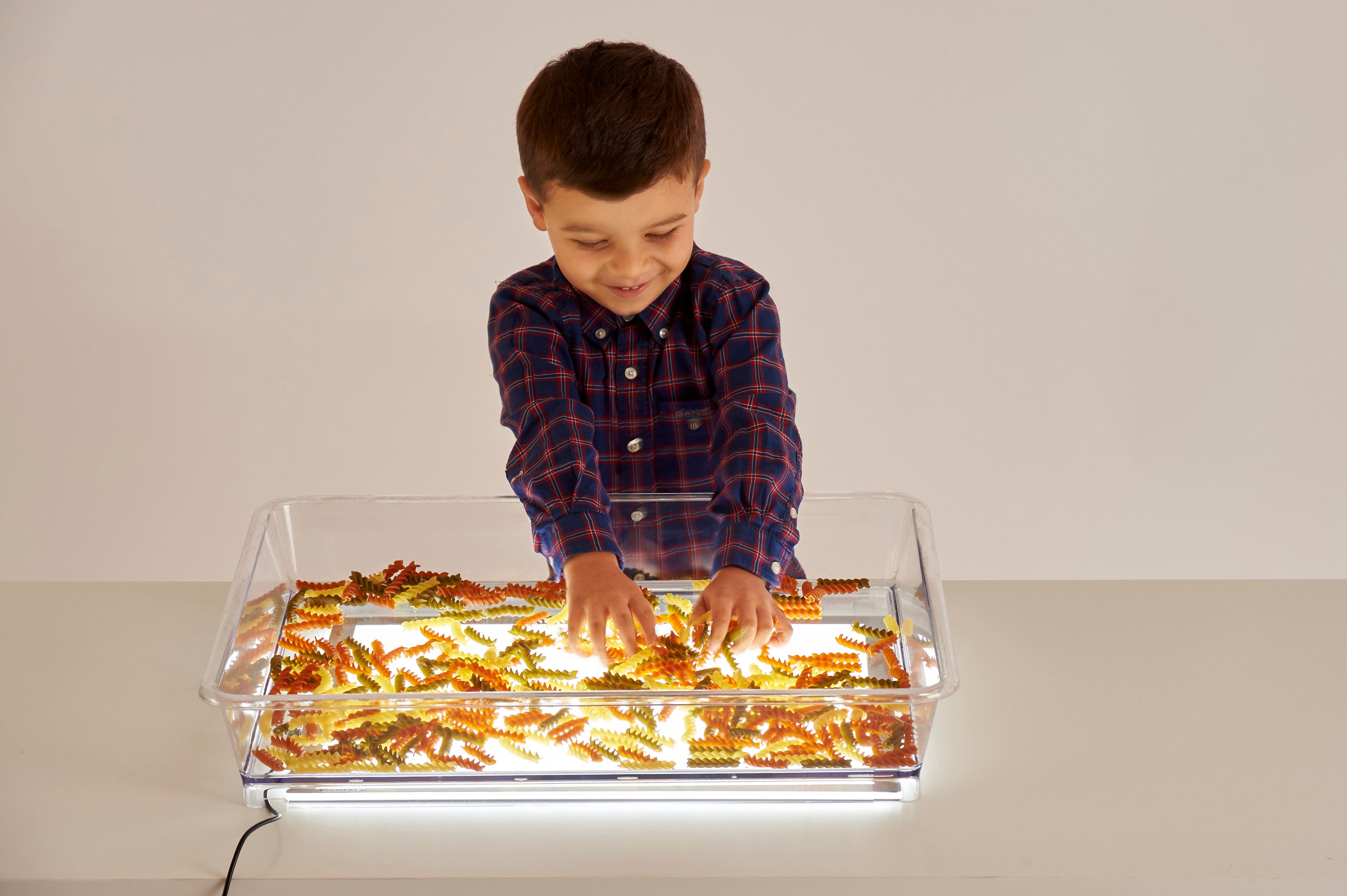 Clear light-up art tray with child hands arranging golden craft pieces