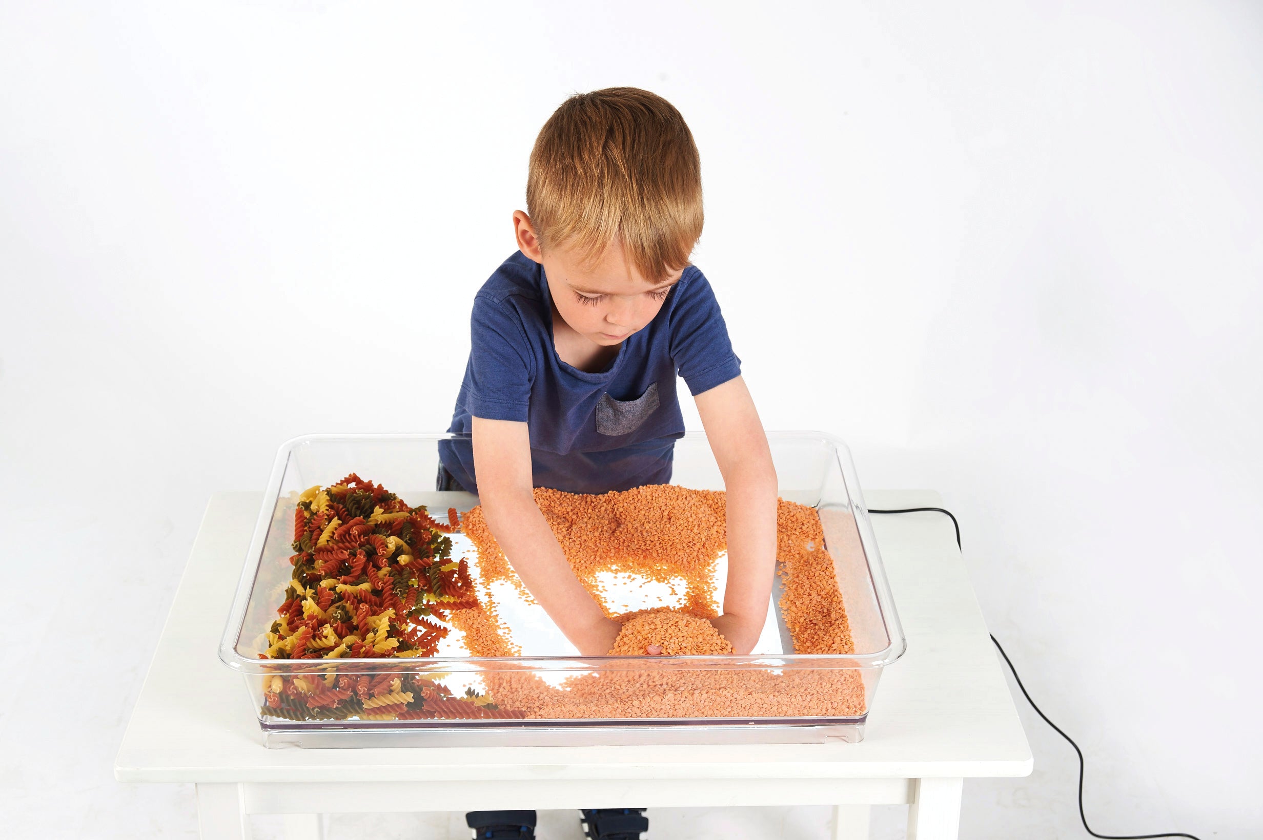 Child arranging items inside a clear tray on a glowing light panel
