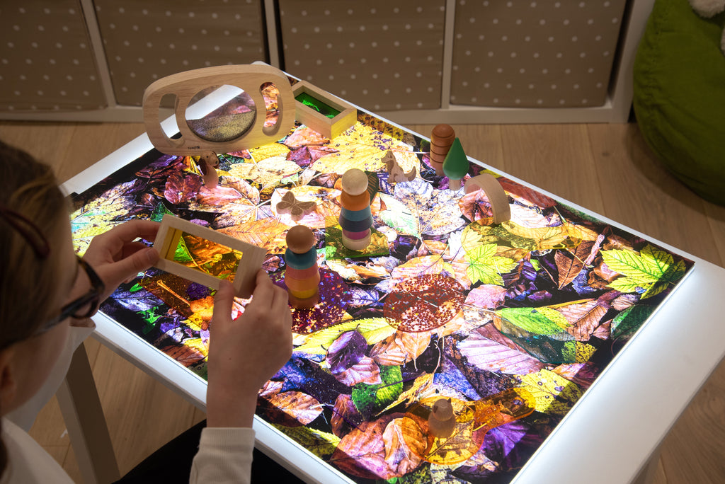 Leaf print play mat on table with hands arranging stacking toys