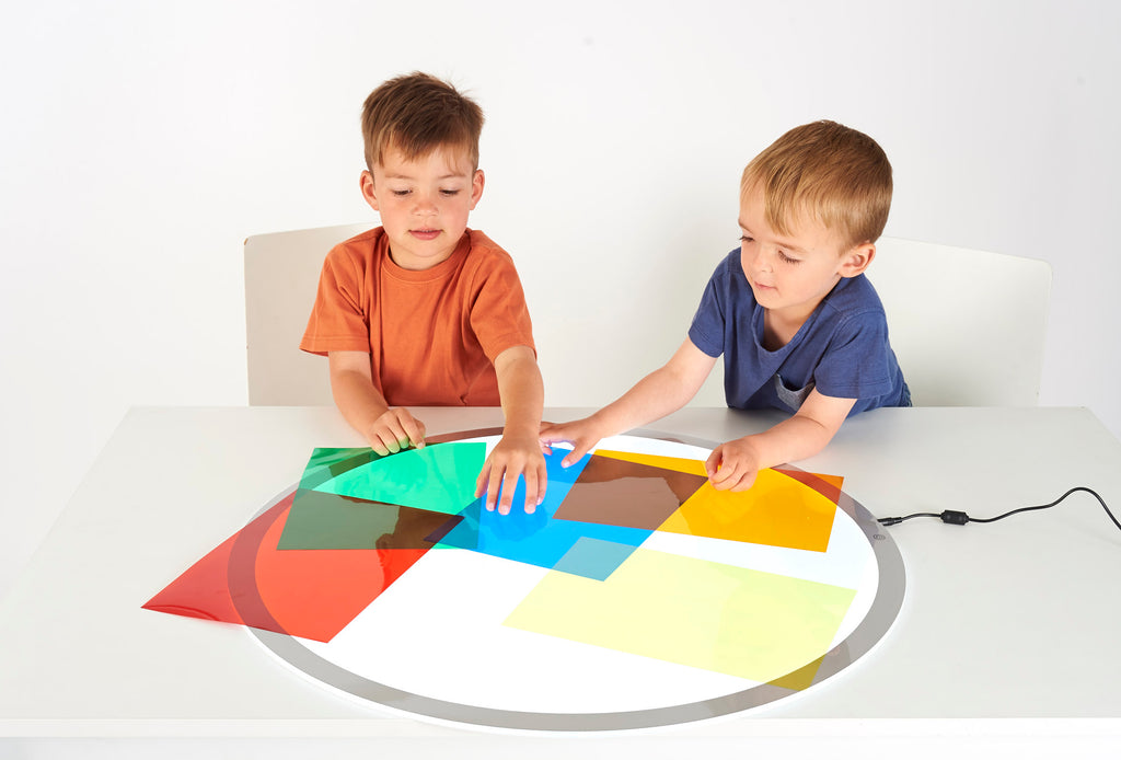 Colored acetate sheets with kids arranging layered transparent panels on a tabletop