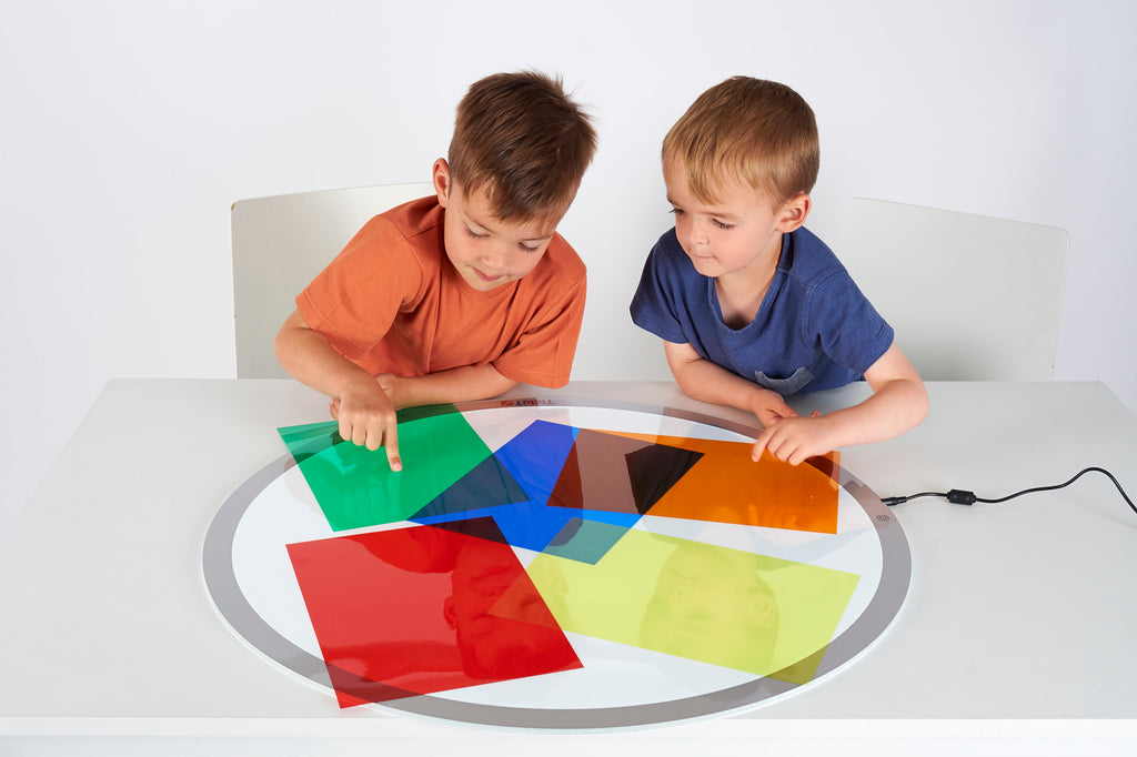 Colored acetate sheets laid out as transparent blocks while kids press and overlap them