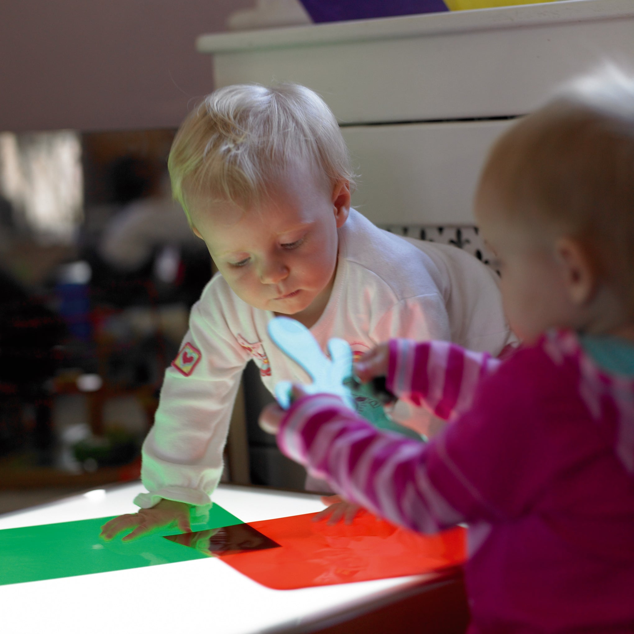 Colored acetate sheets on a table as children reach for red and green transparent pieces