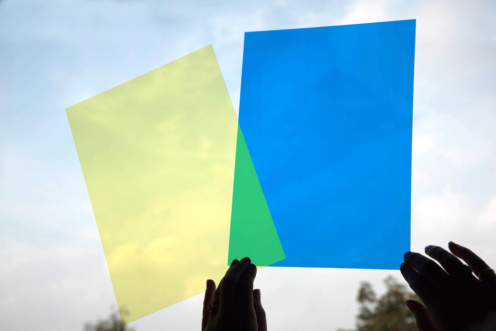 Colored acetate sheets outdoors held up by hands, with blue and light green panels