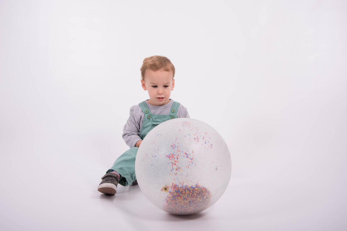 White inflatable ball with multicolor confetti speckles, held by sitting child