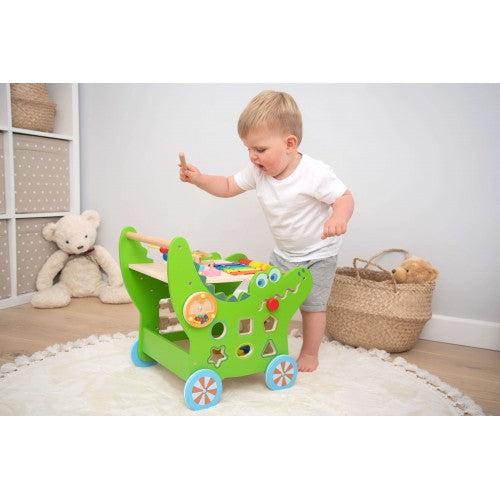 Toddler with green activity walker featuring busy panels, knobs, and blue wheel rims