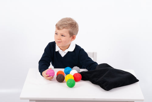 Child holding a pink textured ball with other colorful balls and black pouch nearby