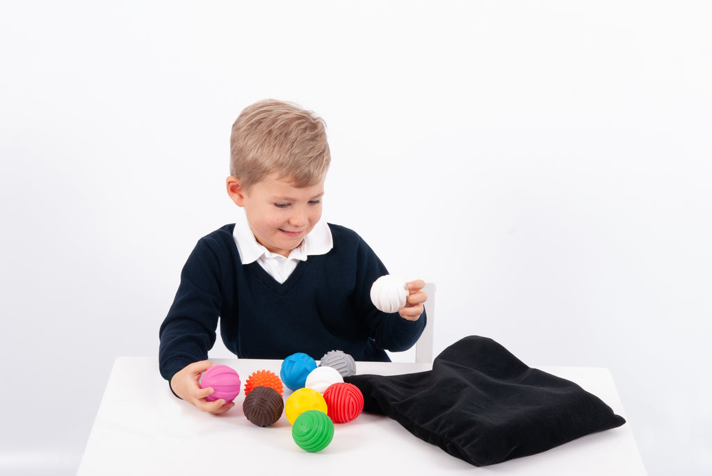 Child with colorful textured balls during play, black pouch on table