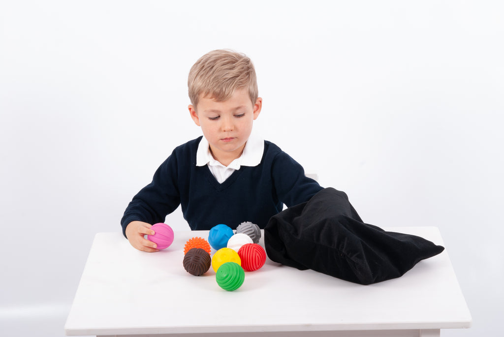 Child grasping colorful textured balls; black pouch lies open on table