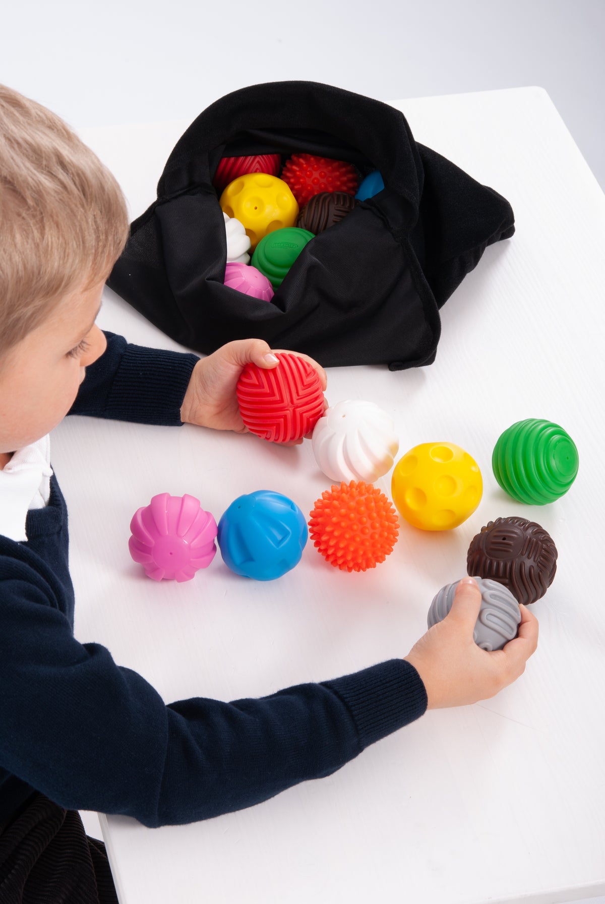 Close-up: child plays with colorful textured balls from open black pouch