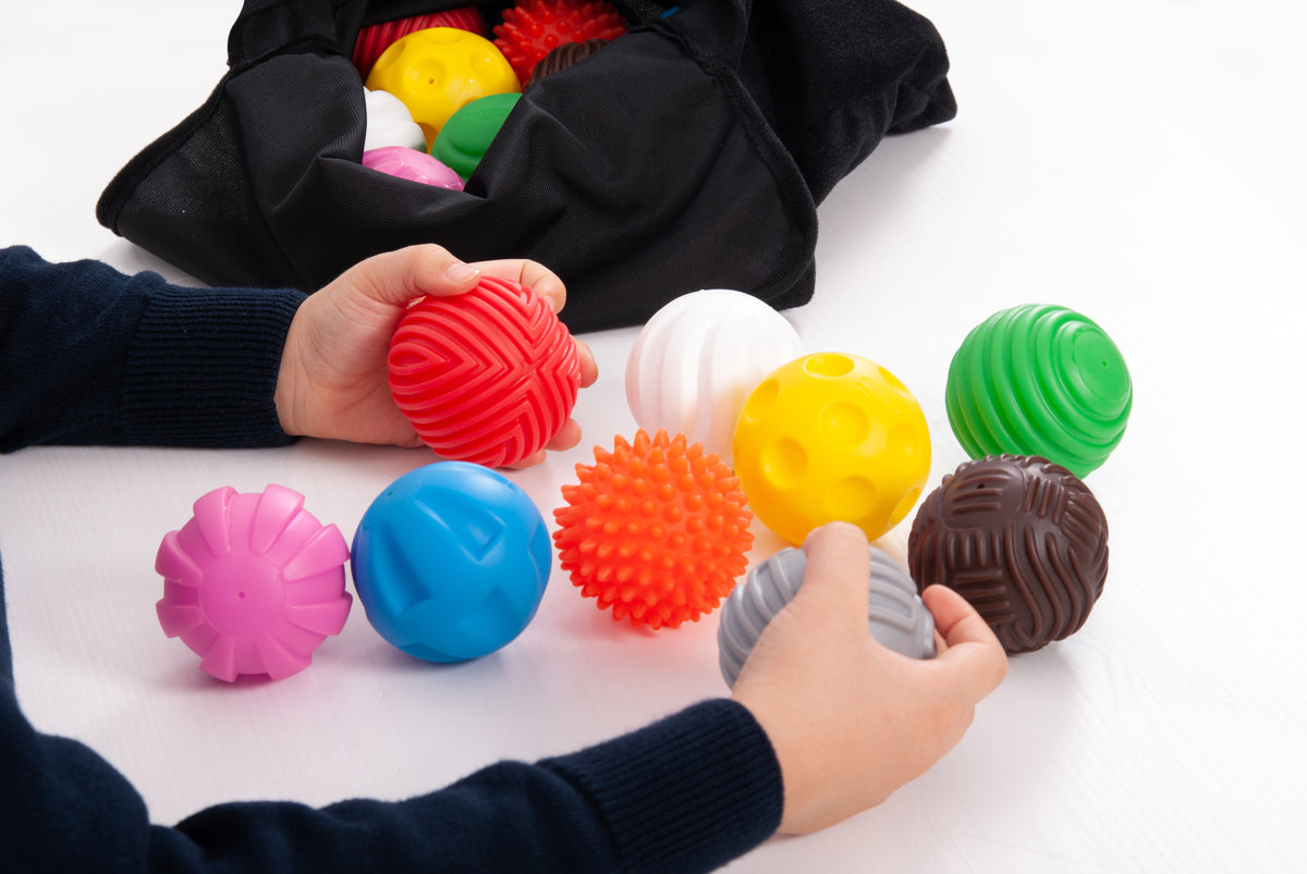 Close-up of colorful textured balls on table with hands reaching, open black pouch