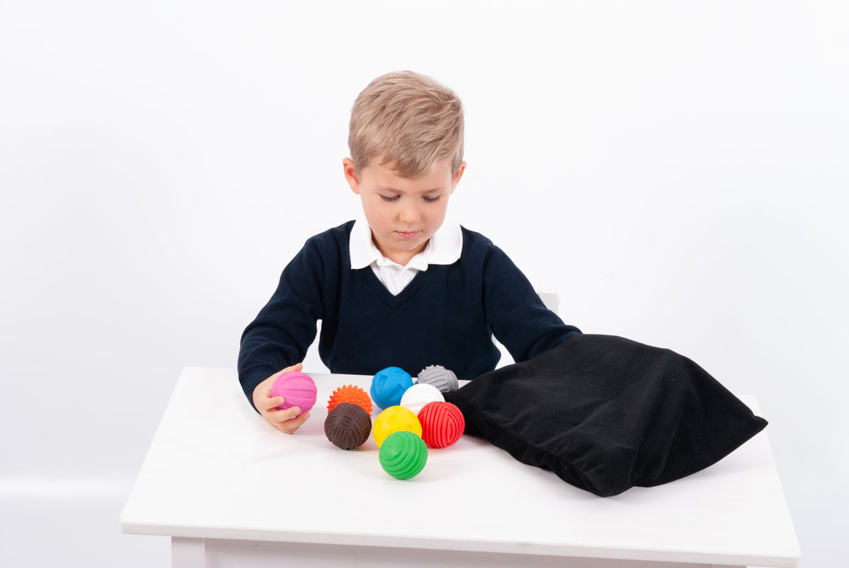 Toddler reaching for colorful textured balls with black pouch draped on table