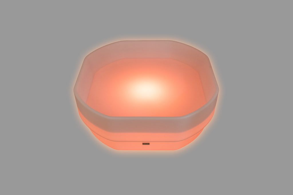 Hexagonal LED glow table with pink-orange light and translucent sides