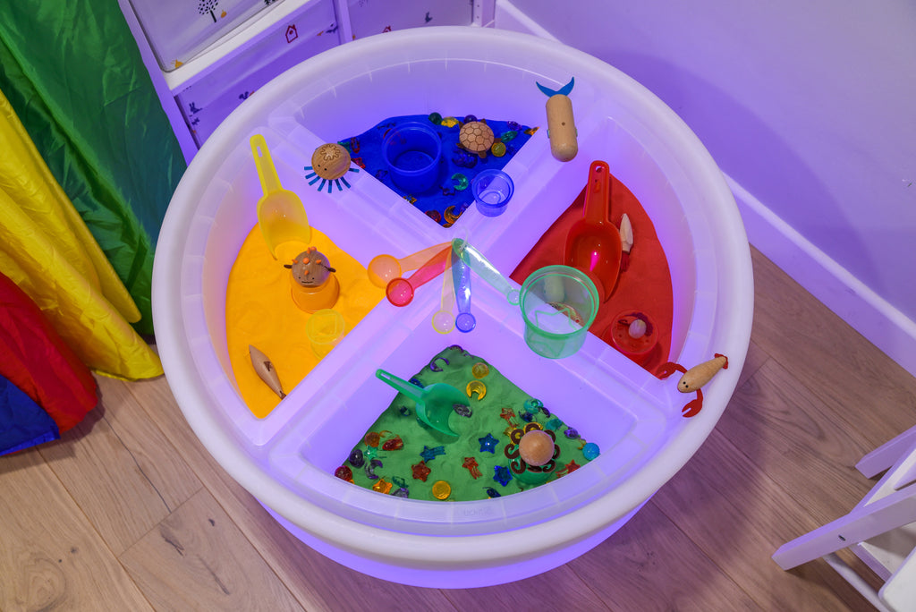 Clear four-compartment round activity tray with partitions, open sections holding toys