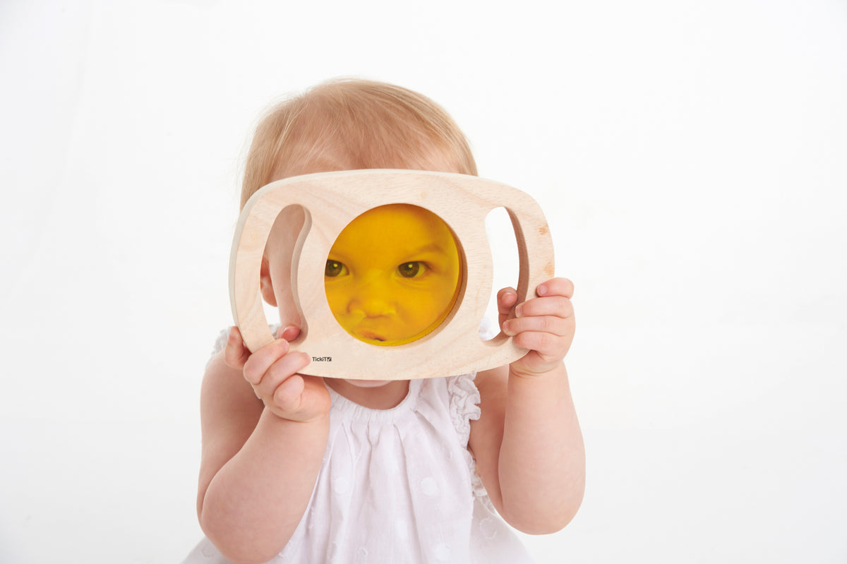 Wooden color panel toy with translucent yellow window held up by a child