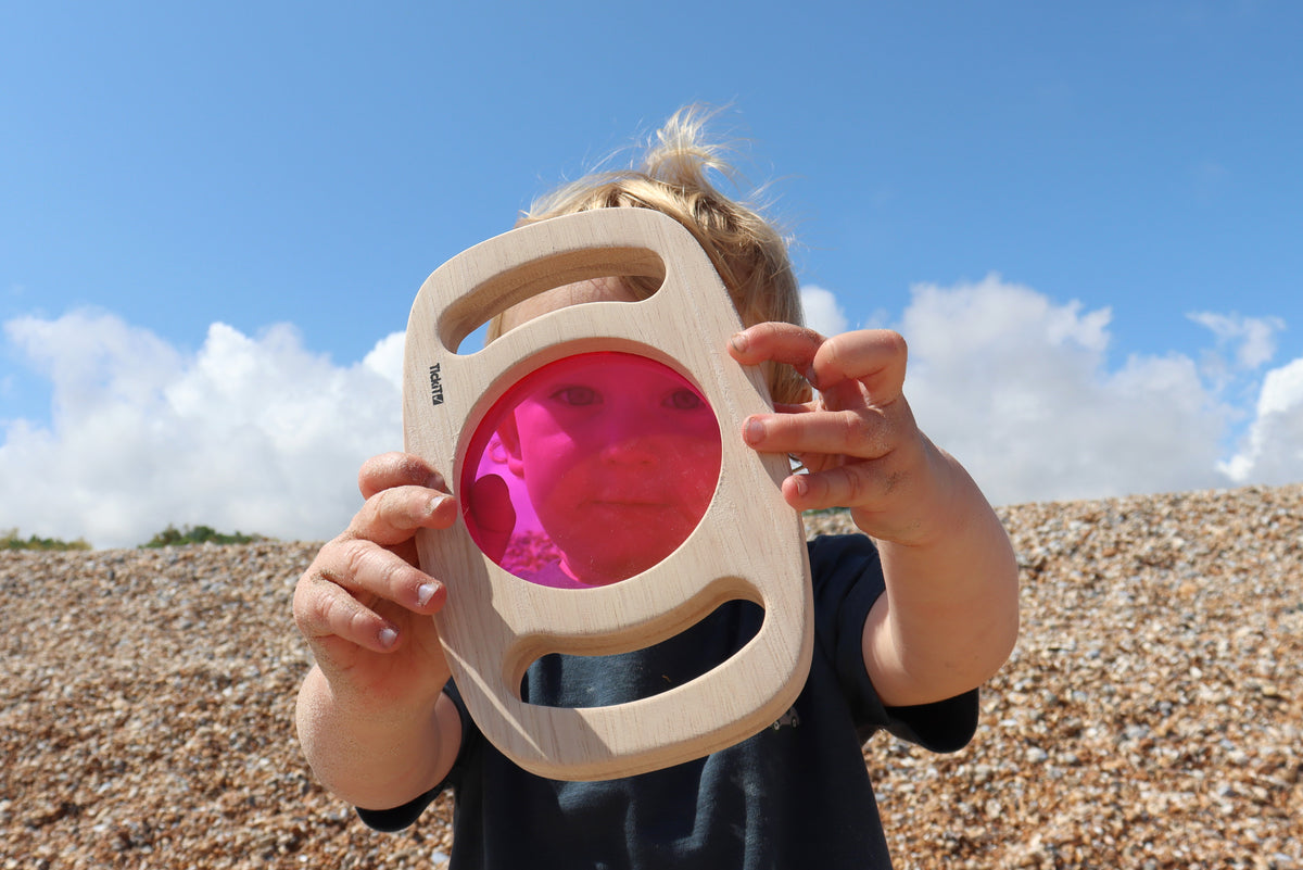 Wooden color panel frame with translucent pink window held to a child’s face