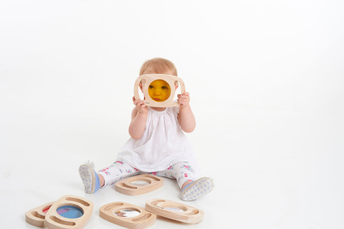 Child wearing a white play hat and holding a wooden sensory face shield with amber window