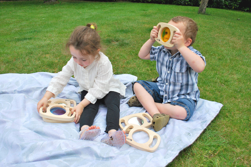 Wooden play sensory frames with colored circular inserts on a cloth, two children playing
