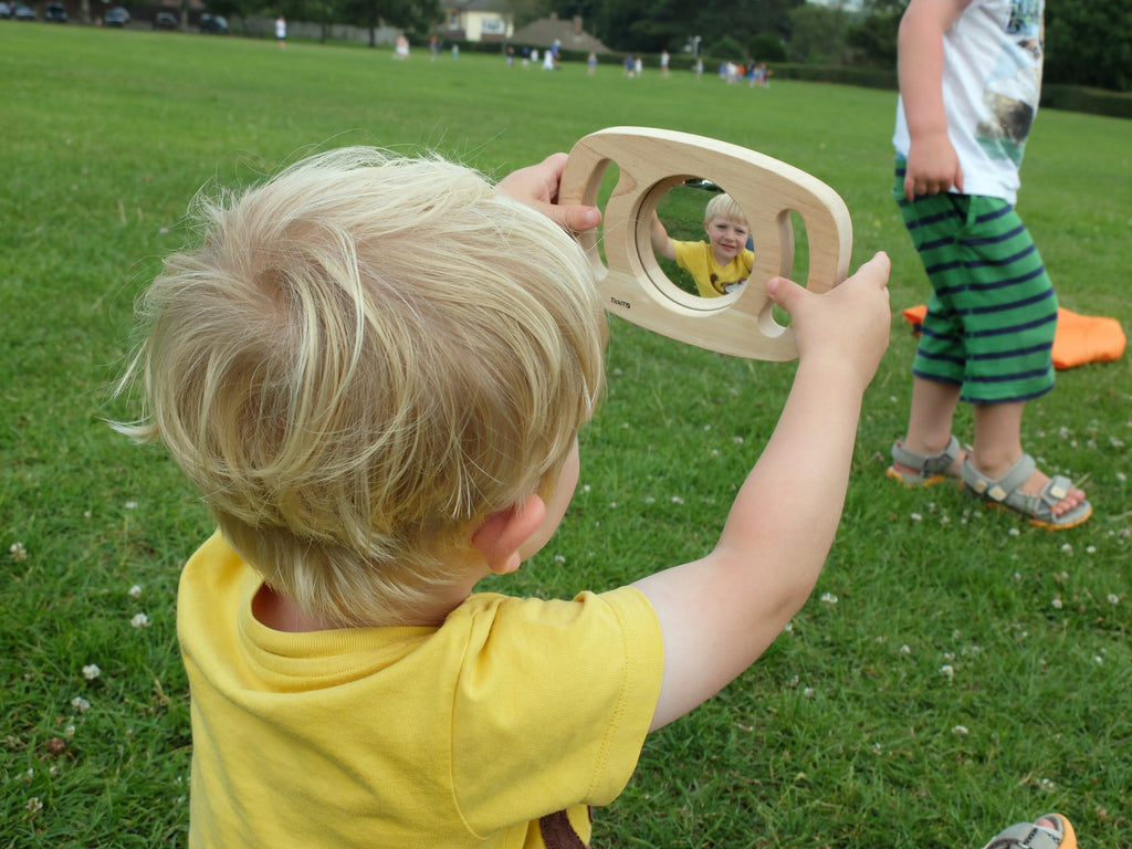 Double-sided mirror toy in light wood oval frame held up outdoors