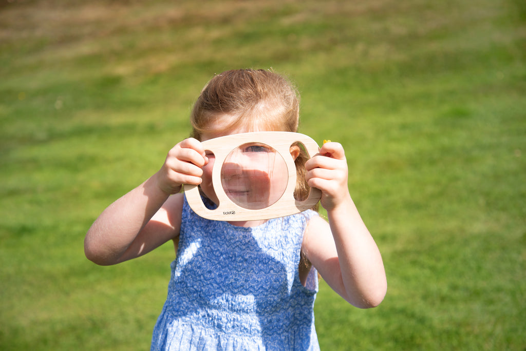 White kaleidoscope toy with circular blue viewing lens, child smiling while looking