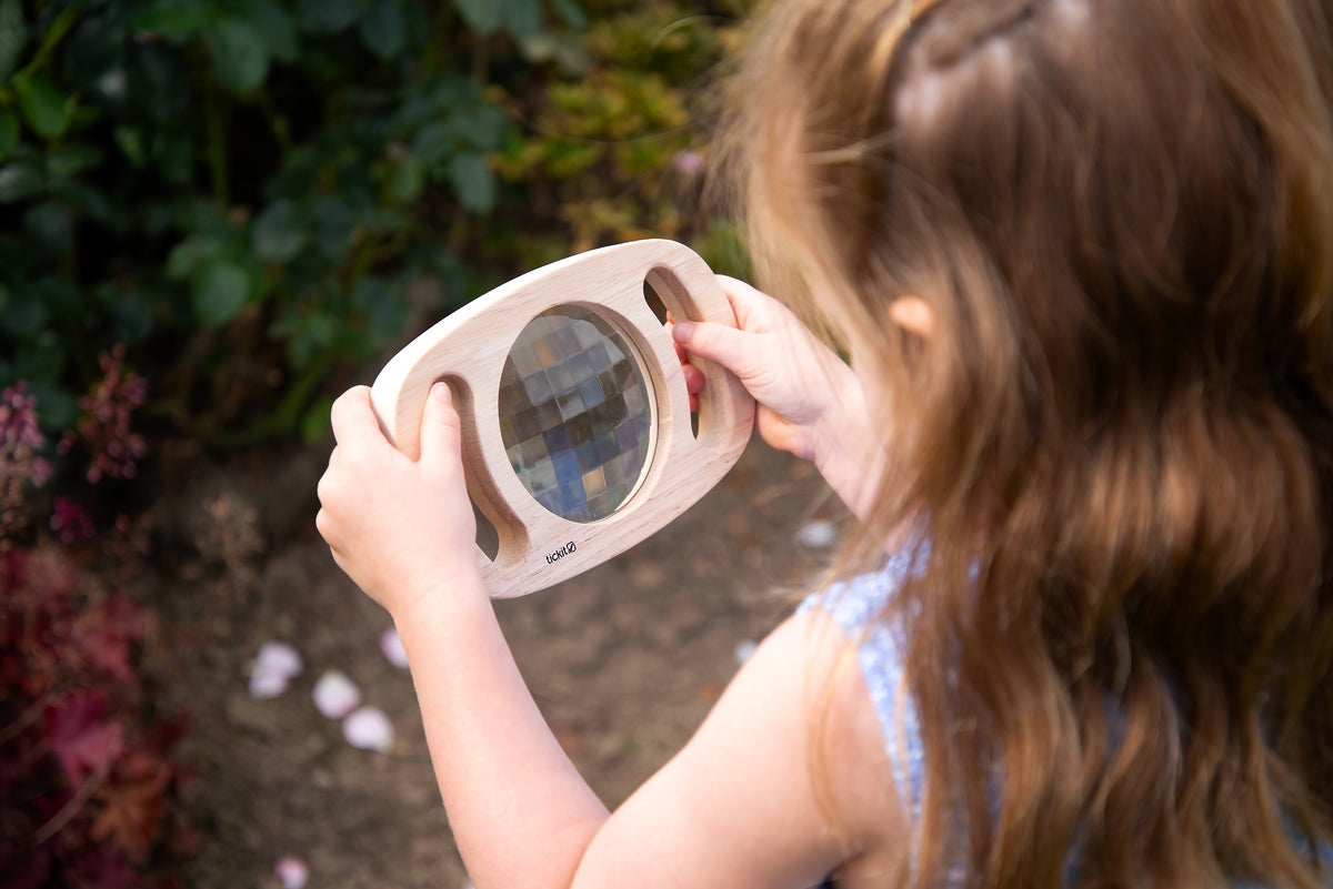 White kaleidoscope toy with circular blue viewing lens, held by a child