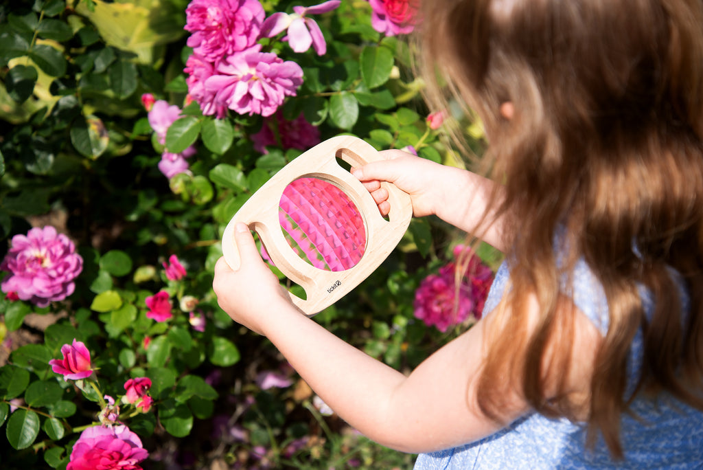 White kaleidoscope toy with pink patterned viewing lens, held by a child
