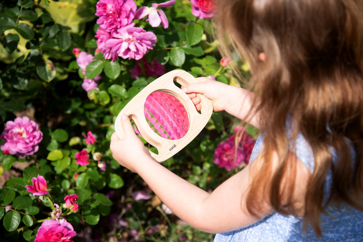White kaleidoscope toy with pink patterned viewing lens, held by a child