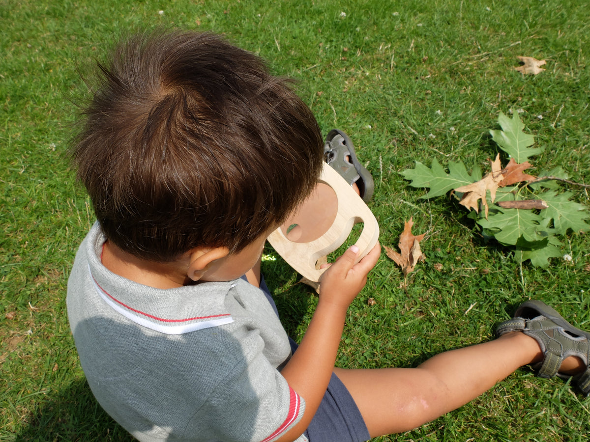 Child holding a wooden magnifier with round lens close to face