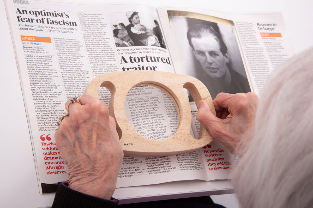 Wooden handheld magnifier with round lens over an open book page