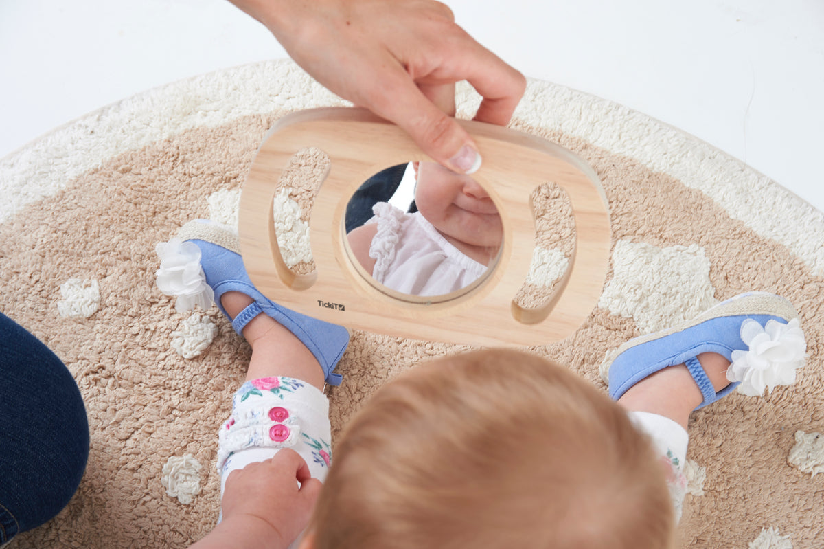 Wooden oval kids mirror with rounded grip, reflecting a child face up close
