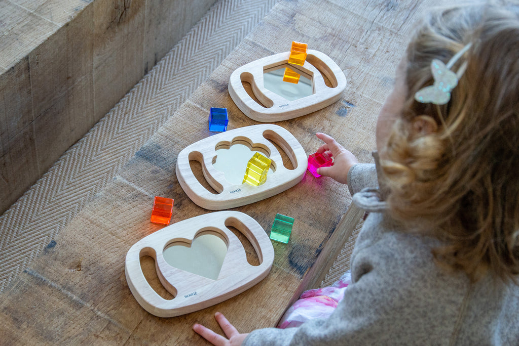 Wooden shape mirror frames with colored pieces; toddler plays on indoor floor