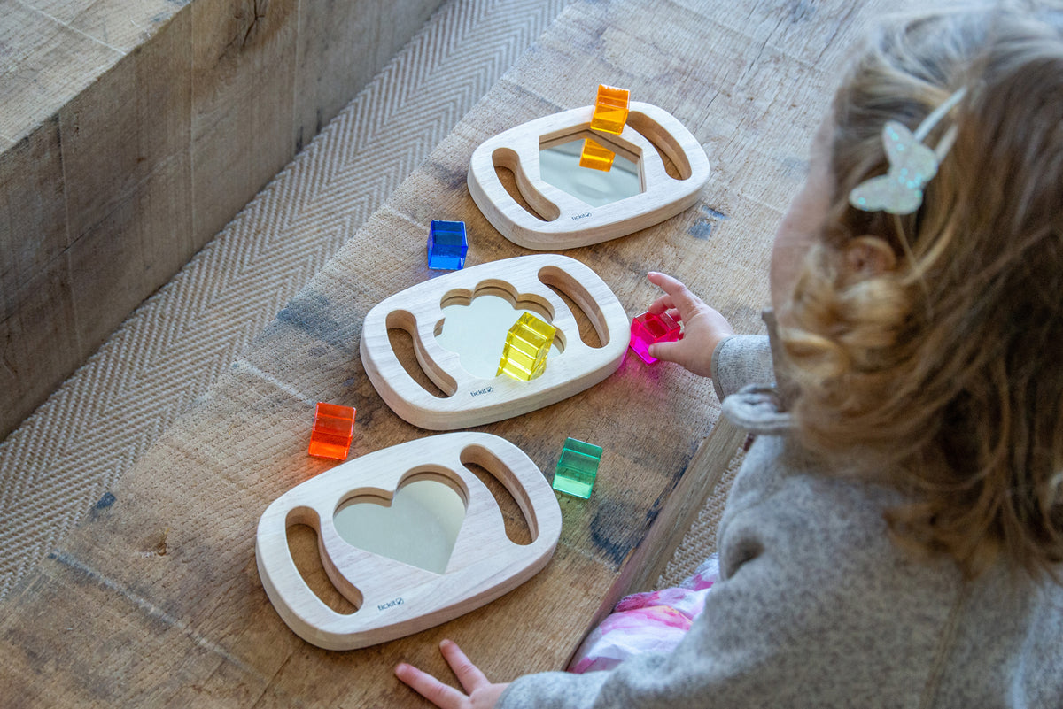 Wooden shape mirror frames with colored pieces; toddler plays on indoor floor