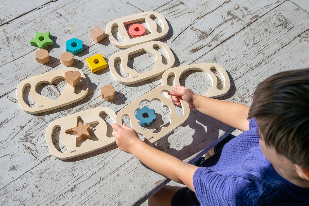 Wooden shape sorter tray with assorted colored pieces including flower, cloud, and star