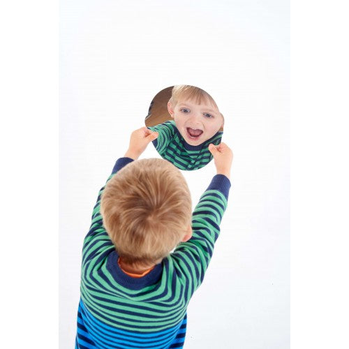 Face-shaped acrylic mirror held by hands, reflecting a child’s face
