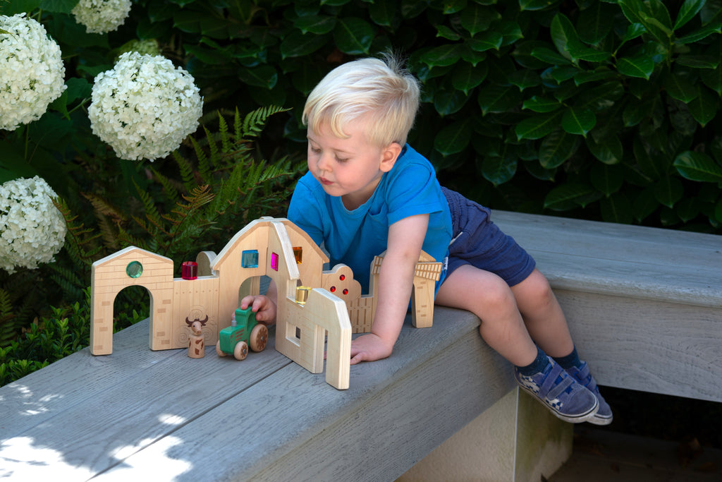 Wooden farm play dividers set while child sits on steps, exploring doors and toys
