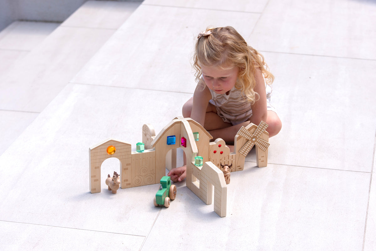 Wooden farm play dividers with child arranging figures, wagon, and toy accessories