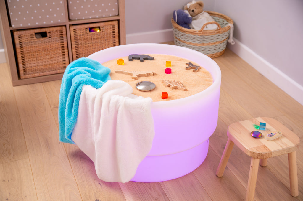 Round sensory play mat with white plush edge, blue and tan inserts, and small toys
