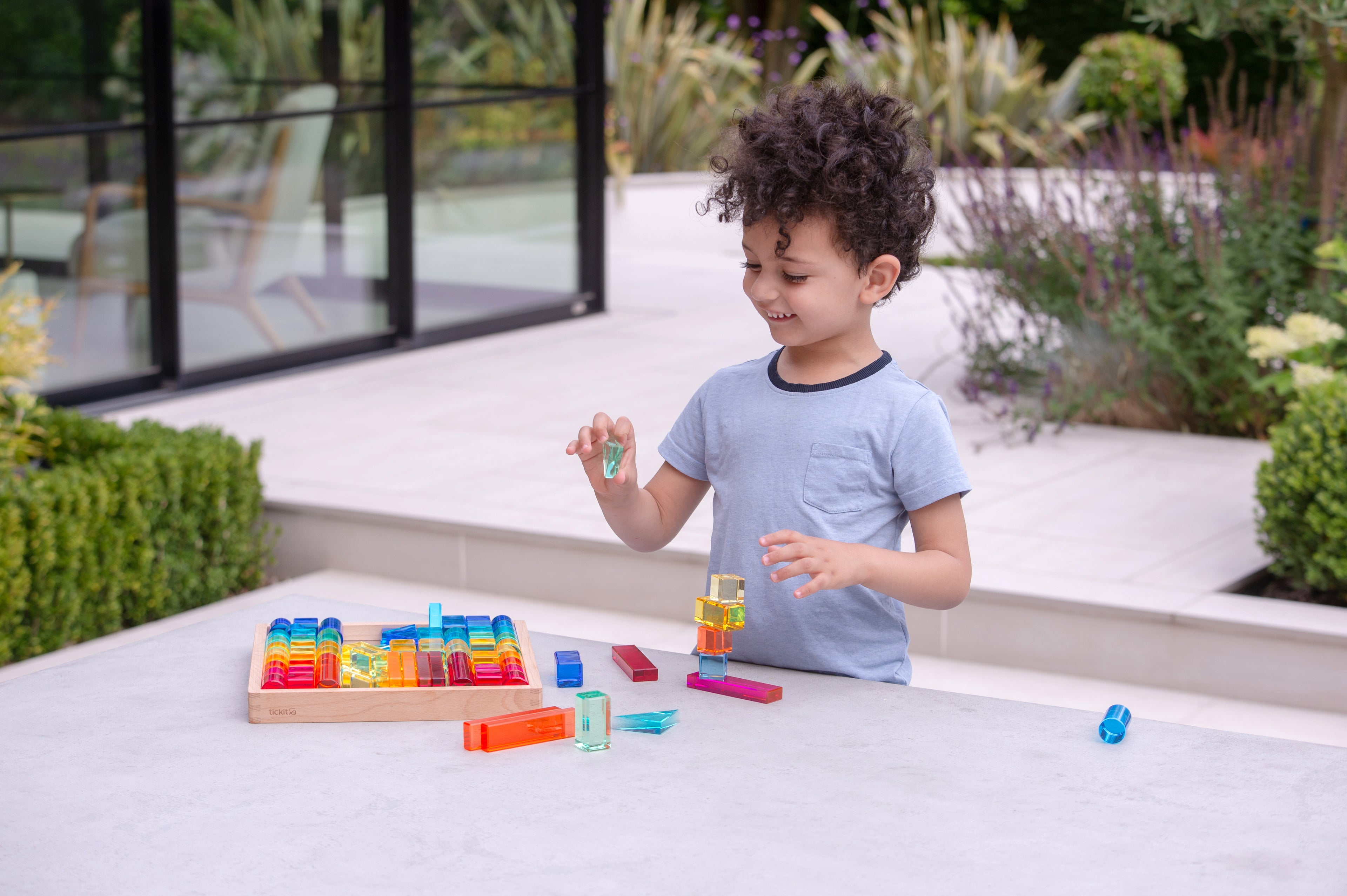 Child holding a colorful gem building piece near a wooden shapes tray